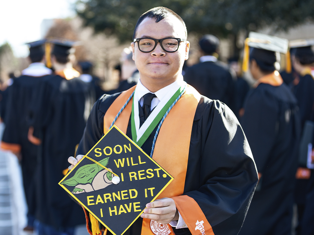 Man holding grad cap that has a drawing of baby yoda and says soon will I rest, earned it I have