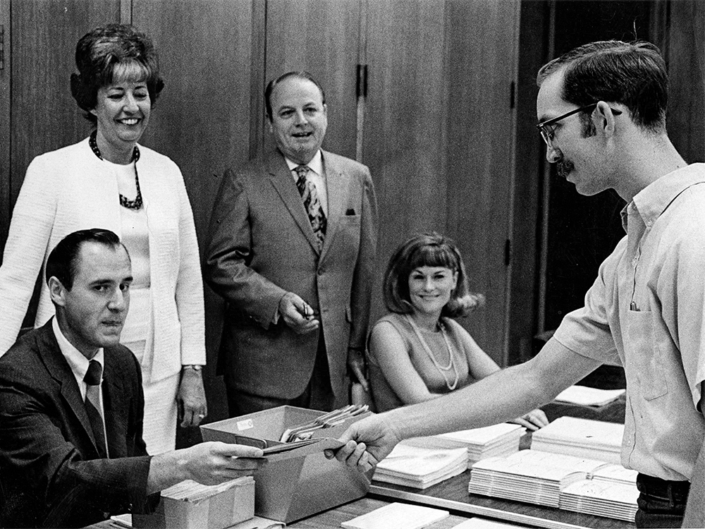 Black and white photo of a student handing a punchcard to a staff member